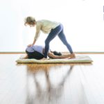 yoga therapy assisted child pose with woman pressing gently on lower back on student doing online yoga therapy training